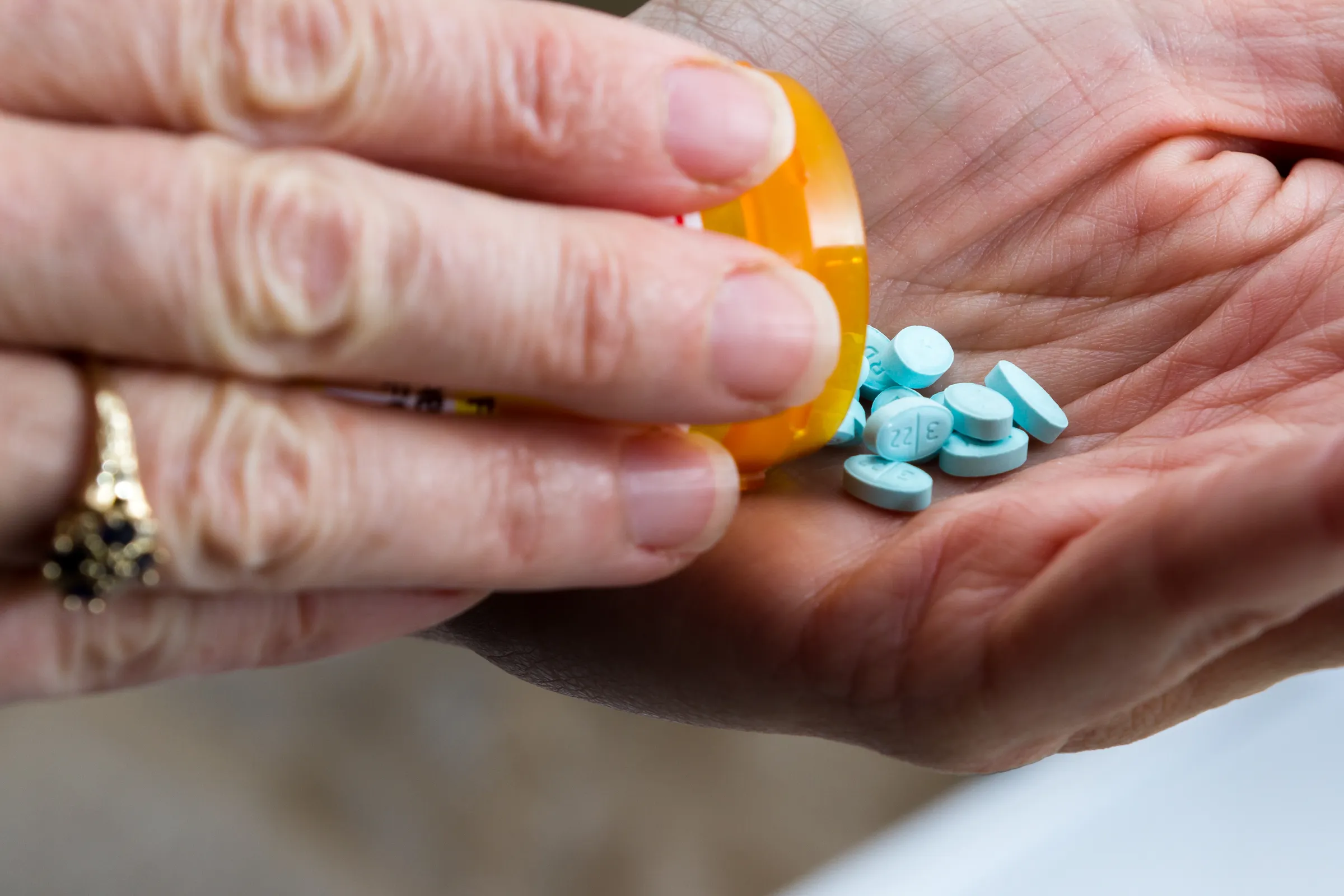 A hand holding a prescription bottle and pills